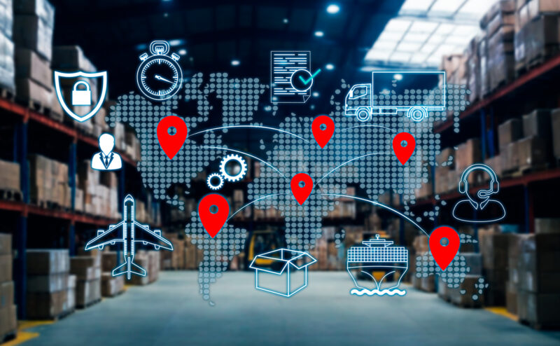 A digitalized global map with pins across it is layered in front of a large storage room. There are stylized logistics icons around the map.